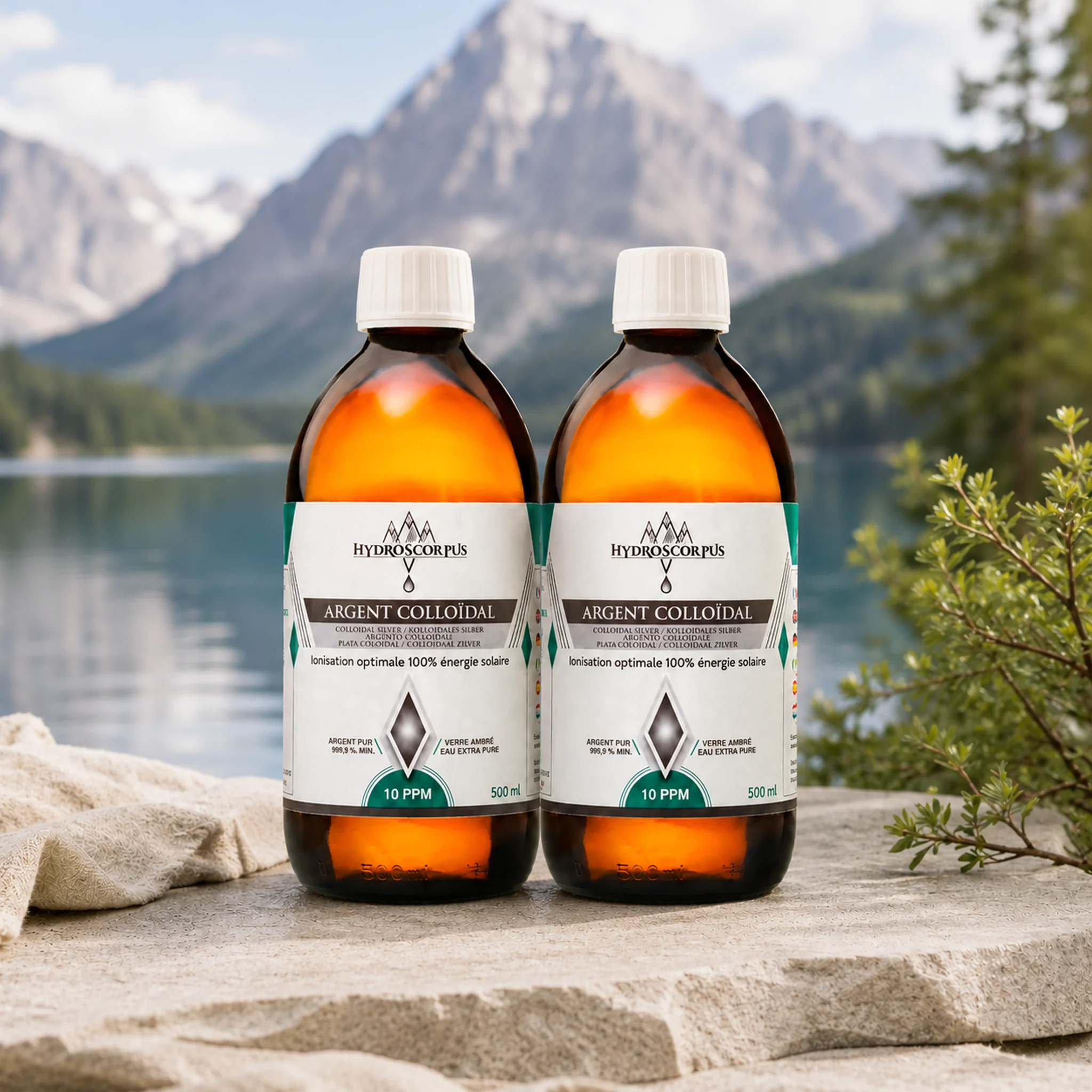 Lot de 2 bouteilles d’argent colloïdal Hydroscorpus 10 PPM en verre ambré 500 ml devant un lac et des montagnes.