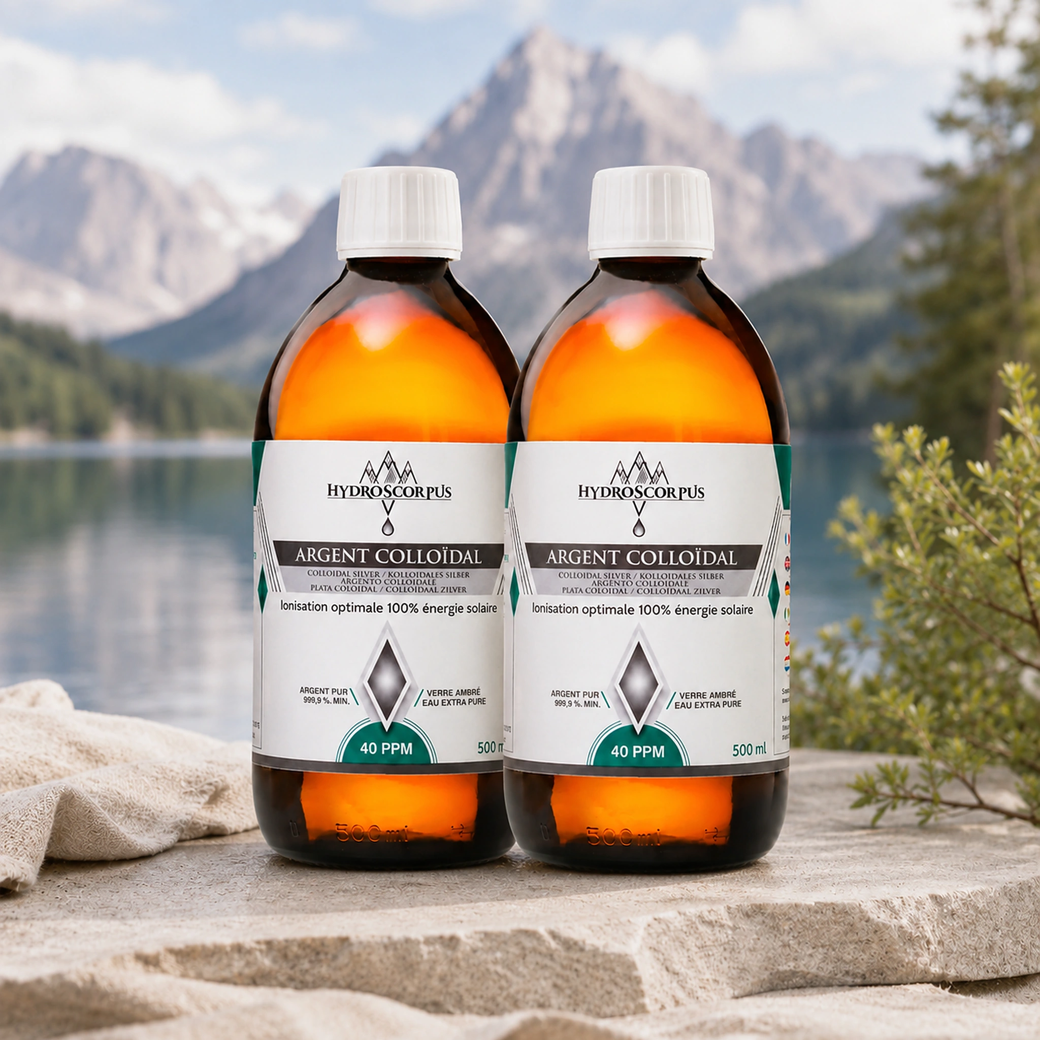 Lot de 2 bouteilles d’argent colloïdal Hydroscorpus 40 PPM en verre ambré 500 ml devant un lac et des montagnes.