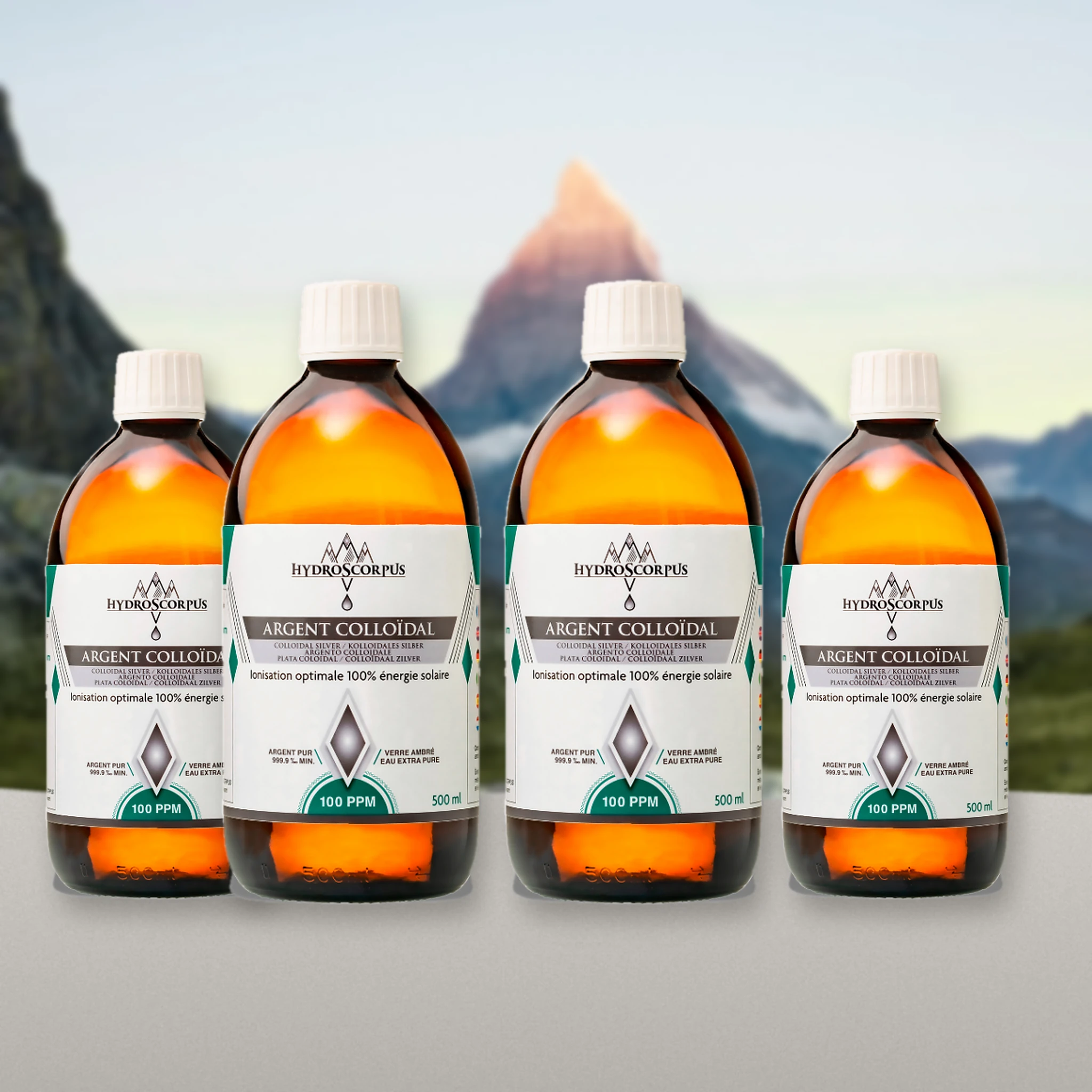 Lot de 4 bouteilles d’argent colloïdal Hydroscorpus 100 PPM en verre ambré 500 ml devant un paysage de montagne.